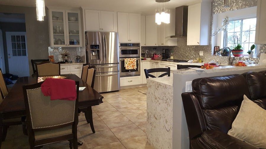 Dining table in foreground with gray patterned cloth draped on chair, and open kitchen with dark cabinets in background.