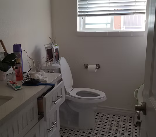 A bright bathroom featuring a white vanity with toiletries, a toilet, and black and white patterned tile flooring.