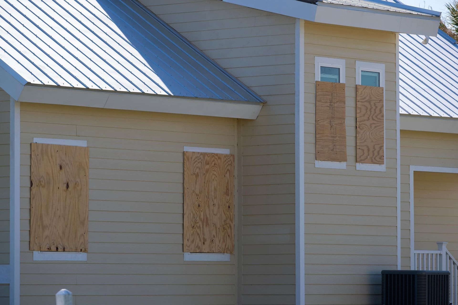 A beige building with a metal roof and its windows covered by plywood boards, likely prepared for a hurricane.