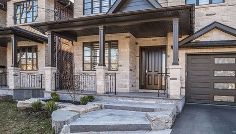the front porch of a brick house with a brown door and steps leading up to it