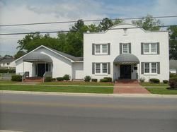 White two-story building with black shutters and arched awning beside a small white house on a street