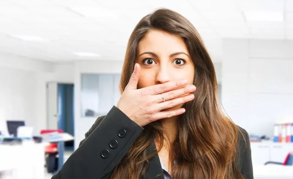 Una donna si copre la bocca in ufficio, con un'espressione sorpresa o scioccata.