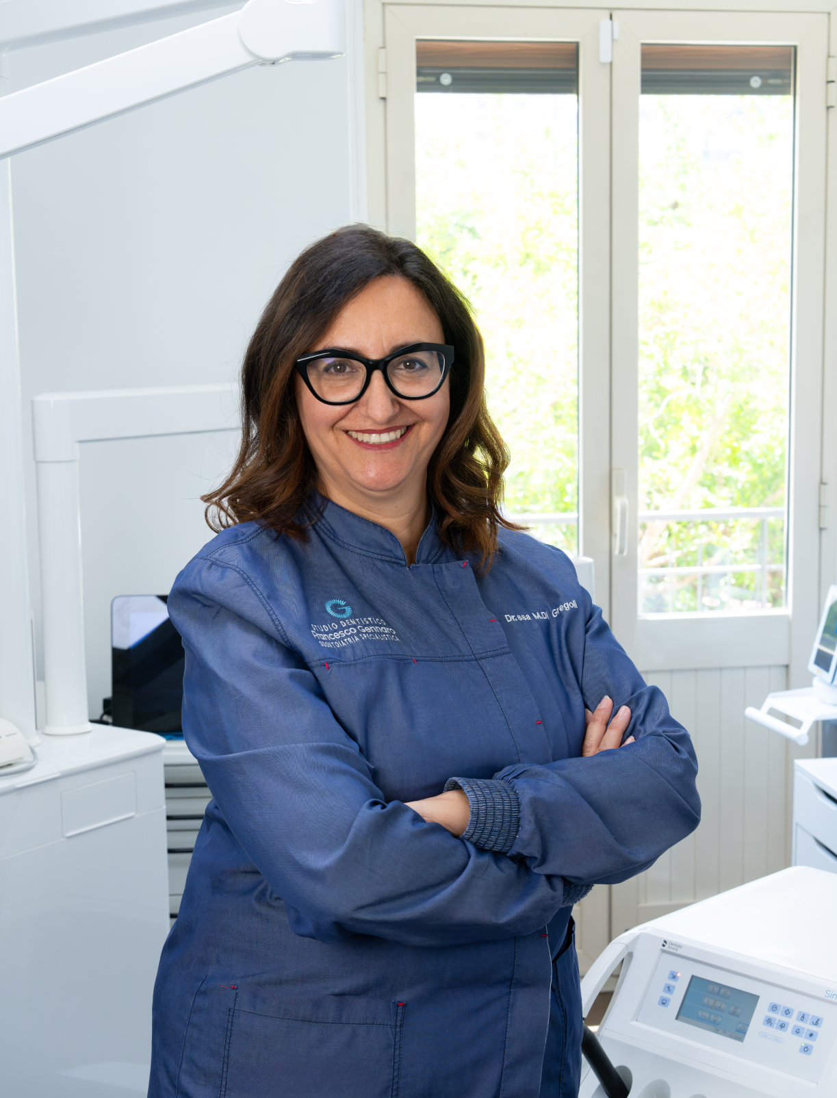 Una persona sorridente in uniforme blu è in piedi davanti a un edificio con una recinzione nera.