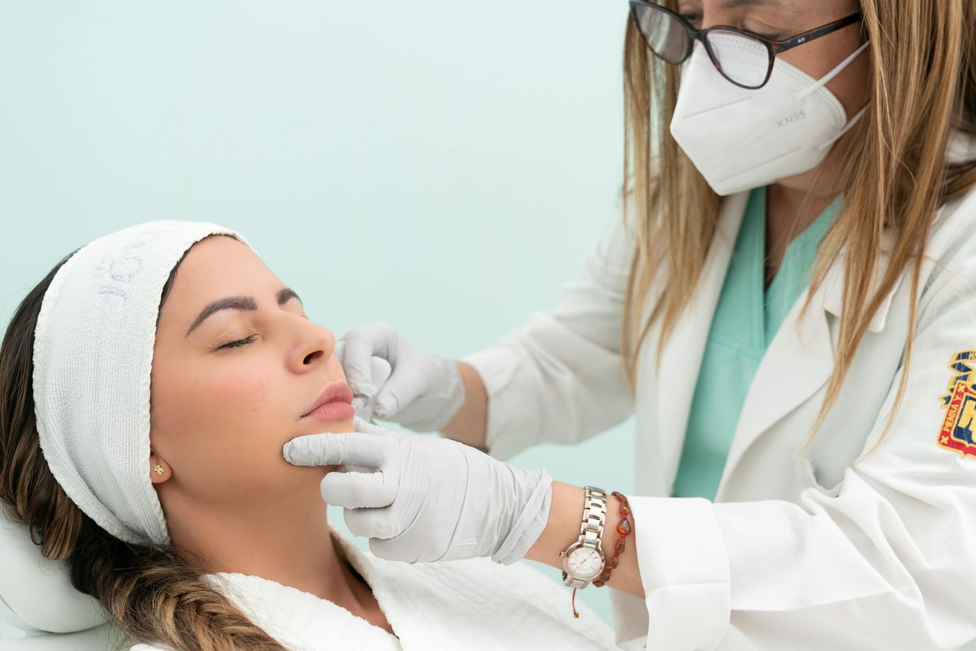Un medico con la mascherina esamina il viso di un paziente durante un trattamento estetico.