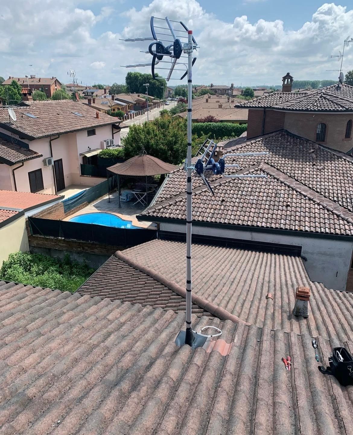 Stazione meteorologica sul tetto di una casa con tetto di tegole, affacciata su una cittadina sotto un cielo nuvoloso.