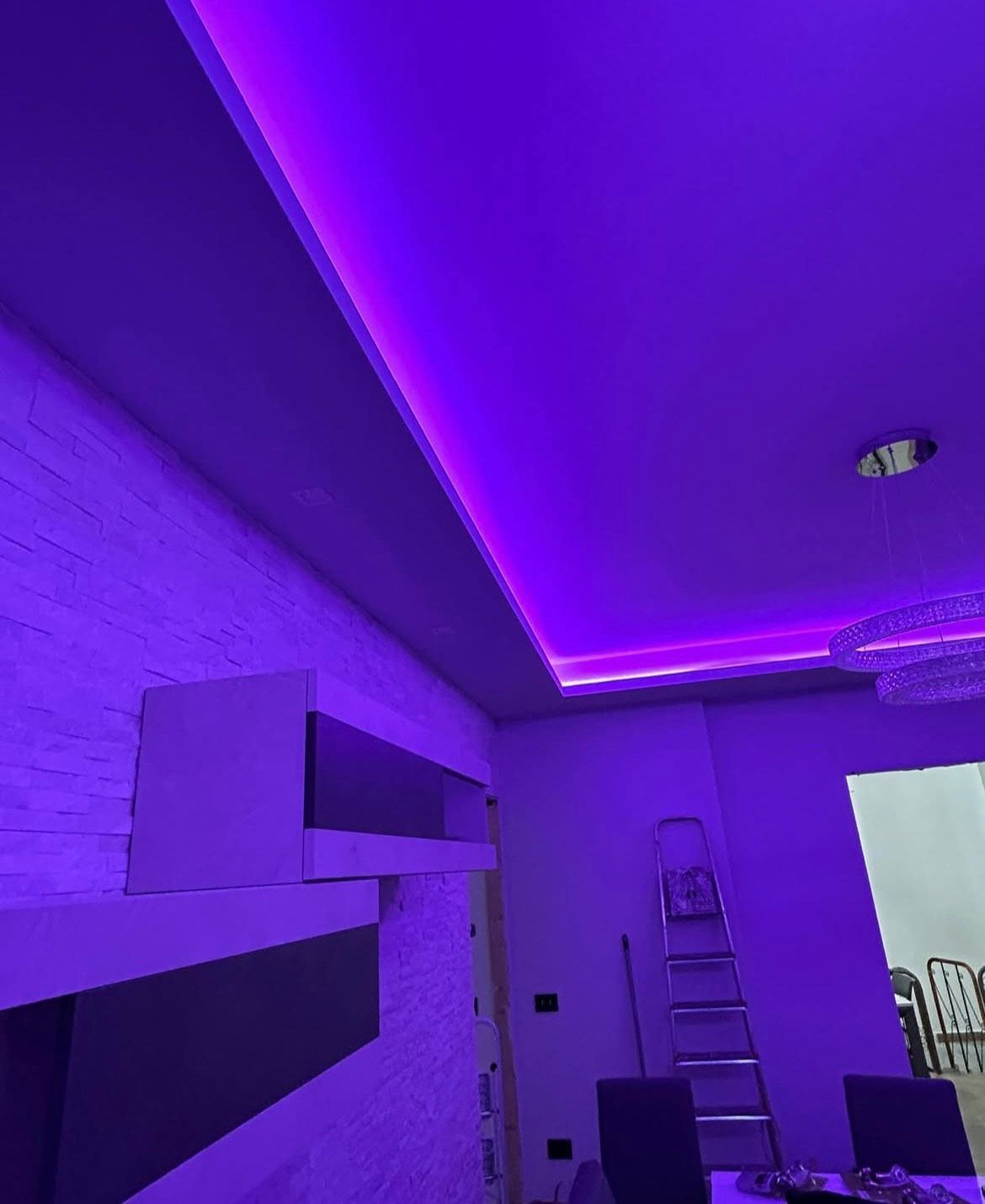 Soffitto della stanza illuminato a LED viola con modanatura a corona, scala e parte di un mobile TV a parete.