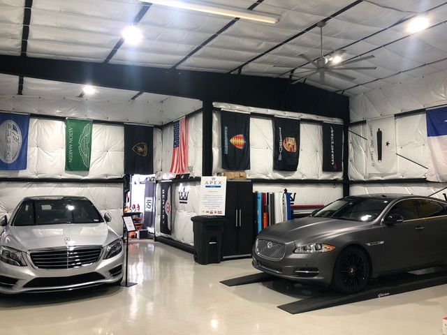 Two cars are parked in a garage with flags on the wall.