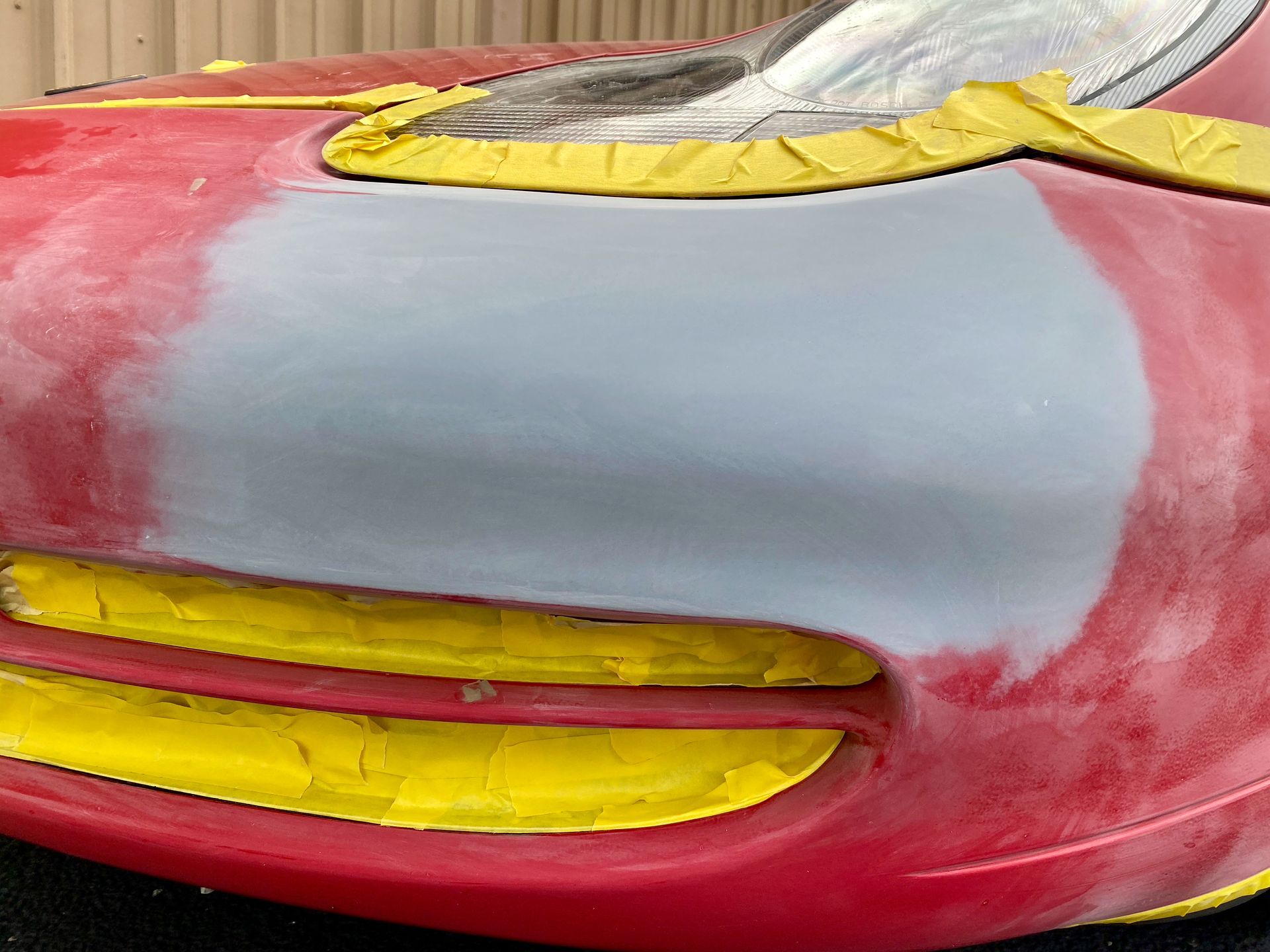 A red car with a yellow stripe on the front is being painted.