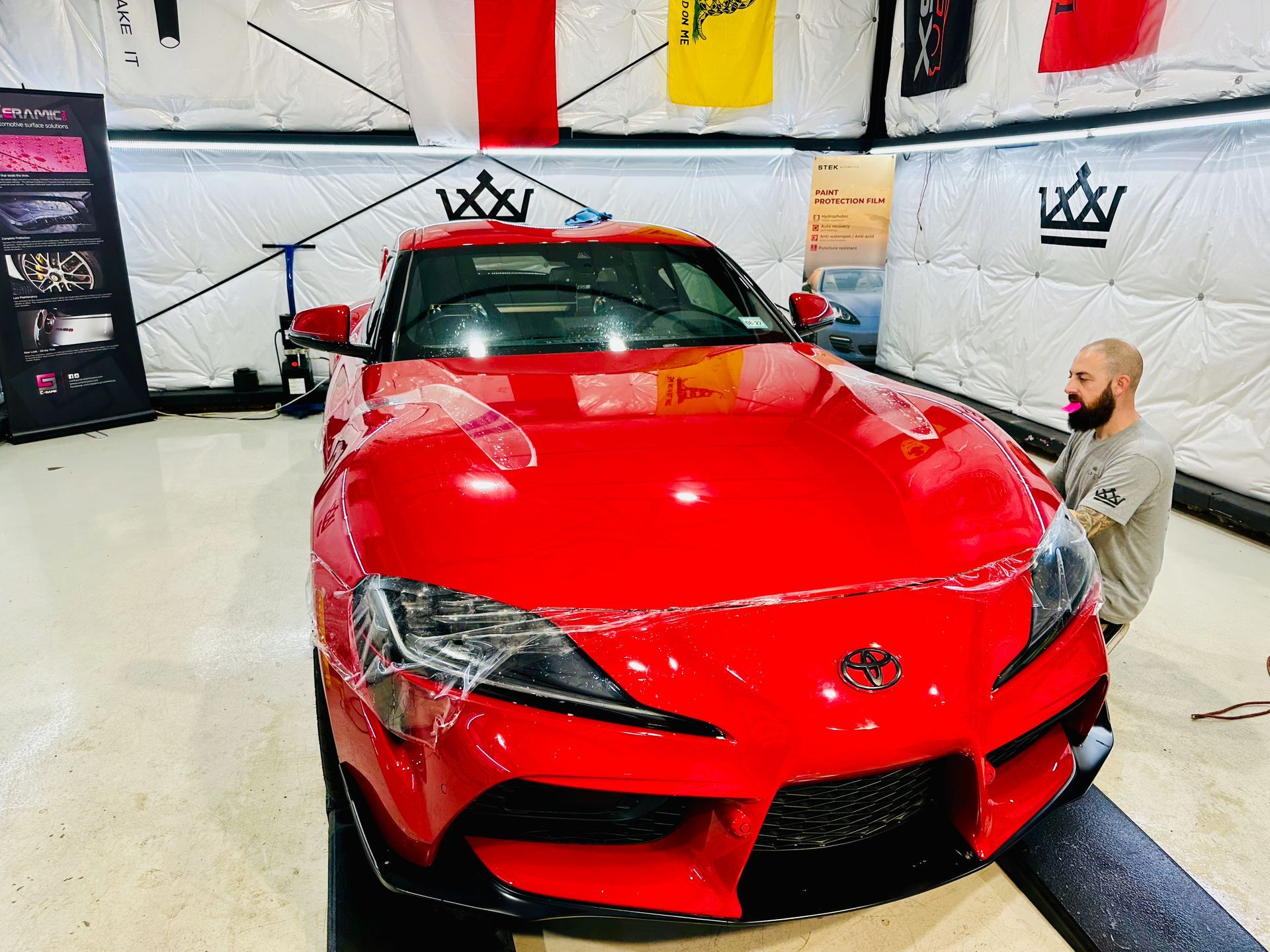 Red sports car in a bright garage, with a person kneeling beside the front bumper.