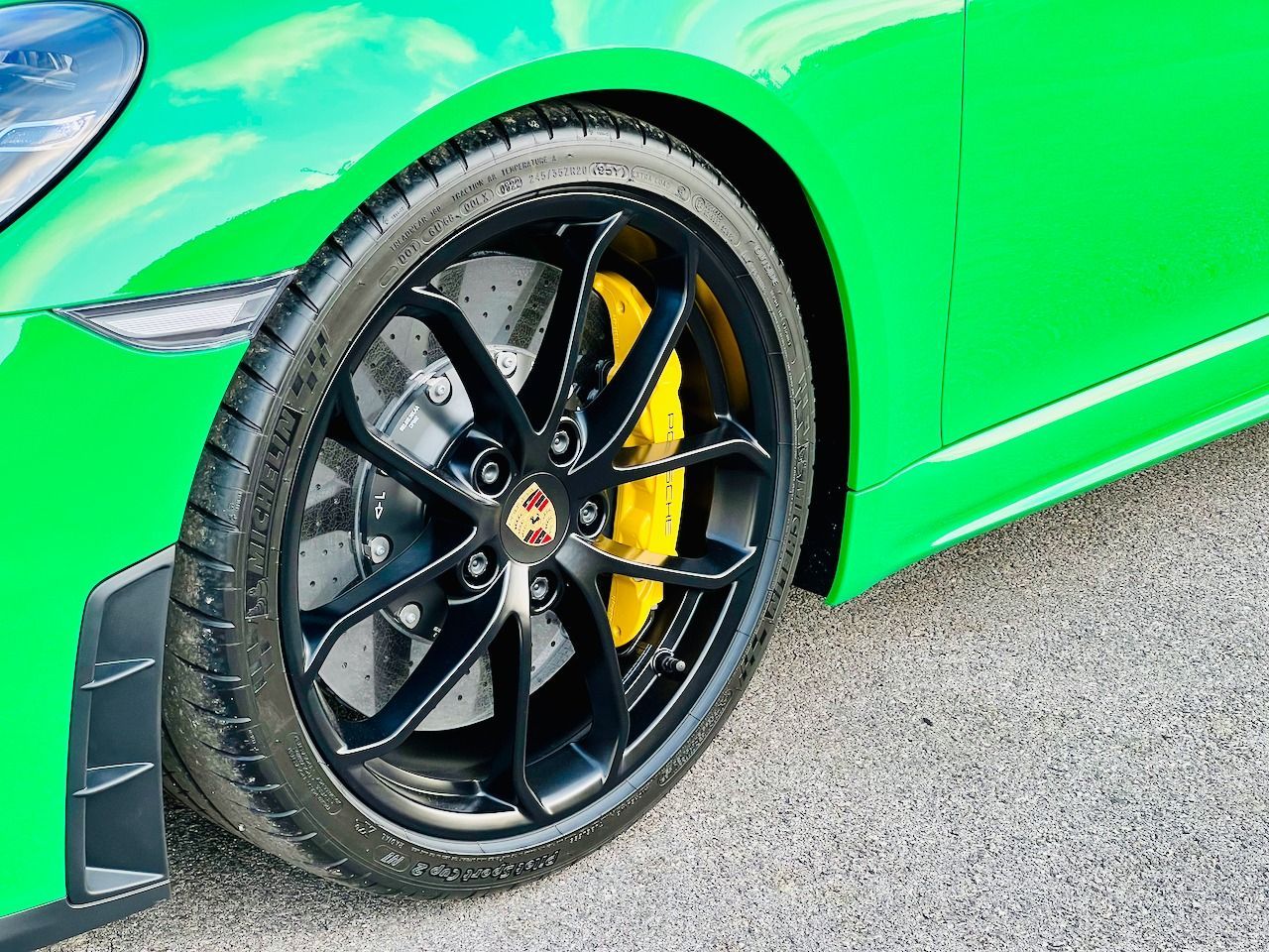 A close up of a green sports car with black wheels and yellow brake calipers.
