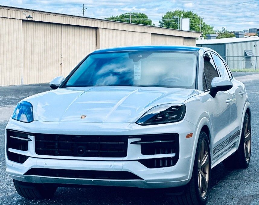 White Porsche SUV parked outdoors beside industrial buildings.