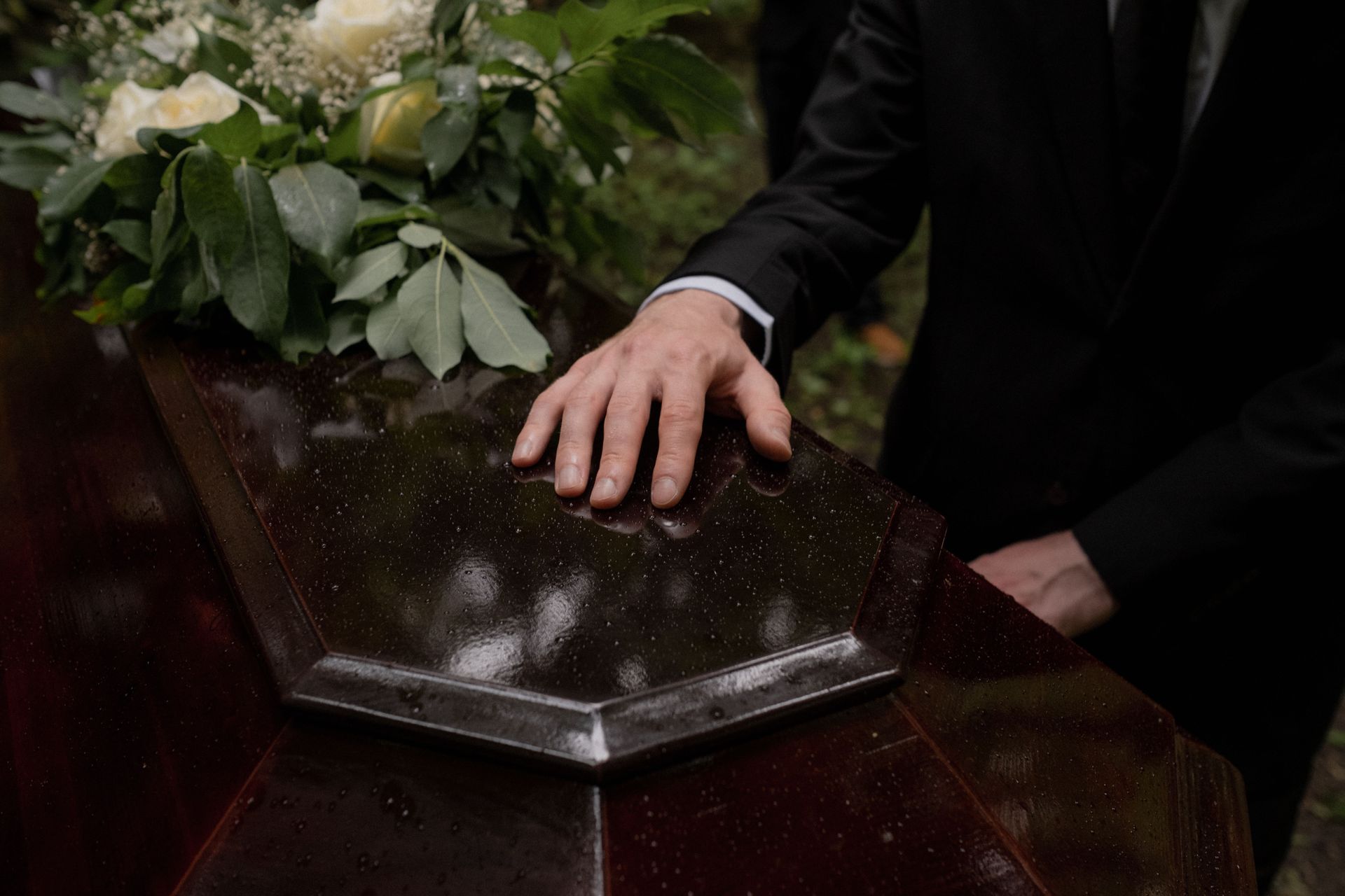 Compassionate funeral home and cremations service in Grand Prairie, TX with family member placing hand on coffin during memorial ceremony.