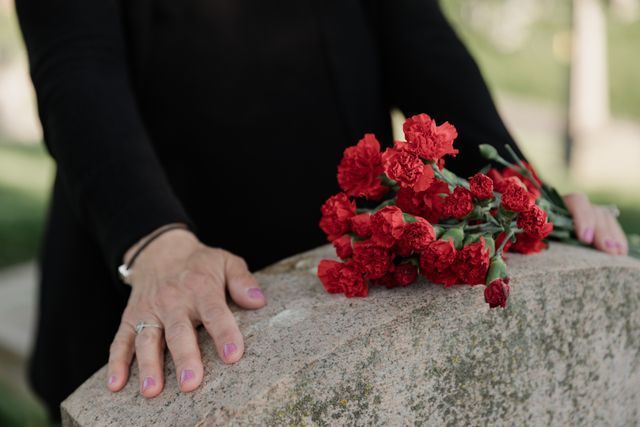 Person standing beside a gravestone with red flowers during a compassionate graveside service in Grand Prairie, TX funeral home and cremations setting.