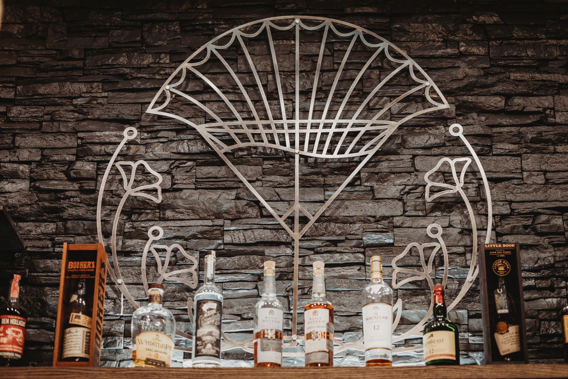 A shelf filled with bottles of liquor and a fan on a brick wall.