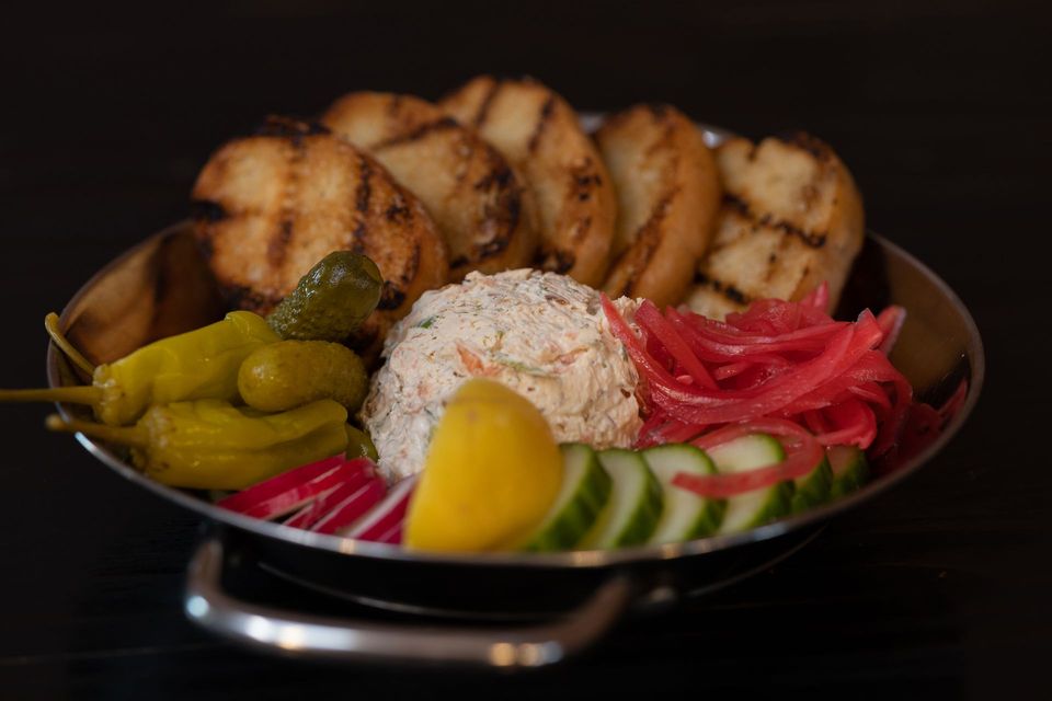 A plate of smoked ruby trout dip with dill, sliced English cucumber, radish, pickled onion, and baguette.