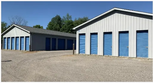 Storage units with blue doors under a blue sky, gravel parking area.