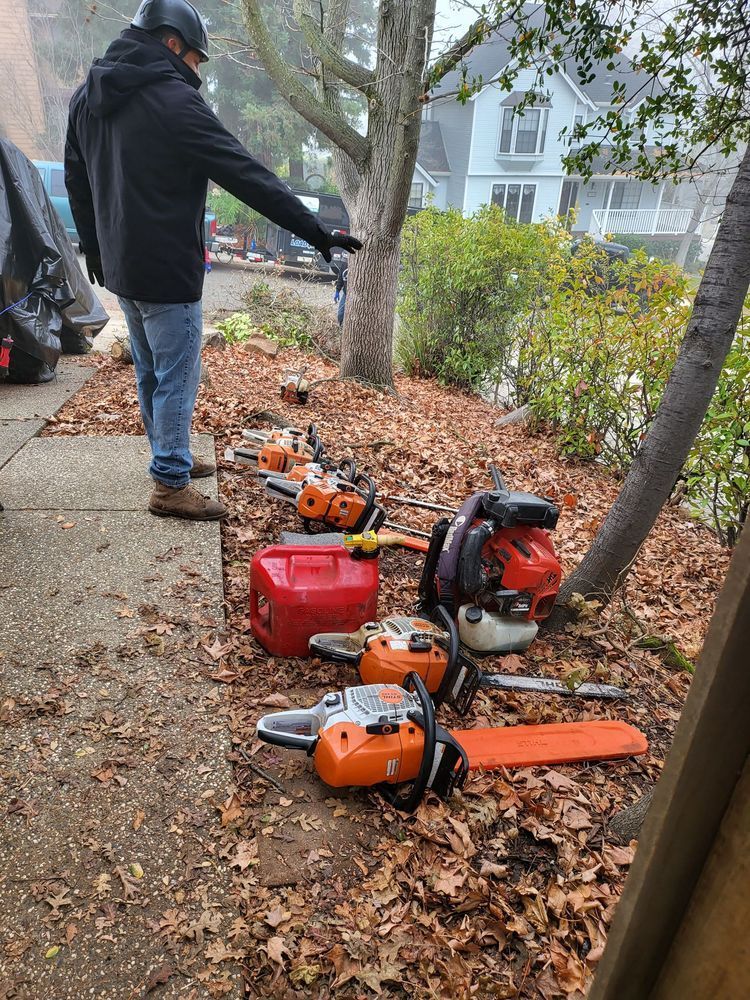 Person using a backpack leaf blower beside several orange yard tools on a leaf-covered sidewalk