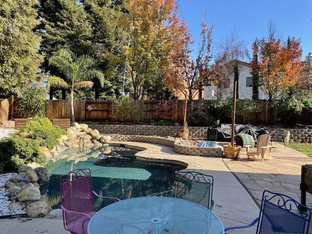 Backyard patio with a pond, stone landscaping, and outdoor chairs under clear blue sky