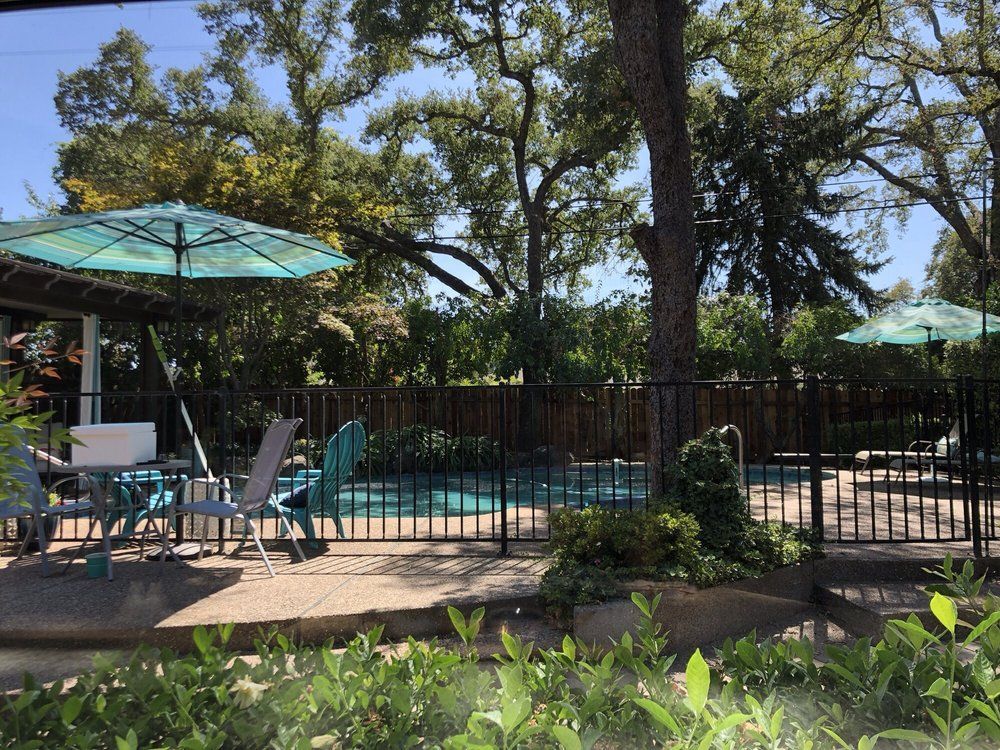 Patio with teal umbrellas, tables and chairs, bordered by a fence and trees in a sunny garden setting