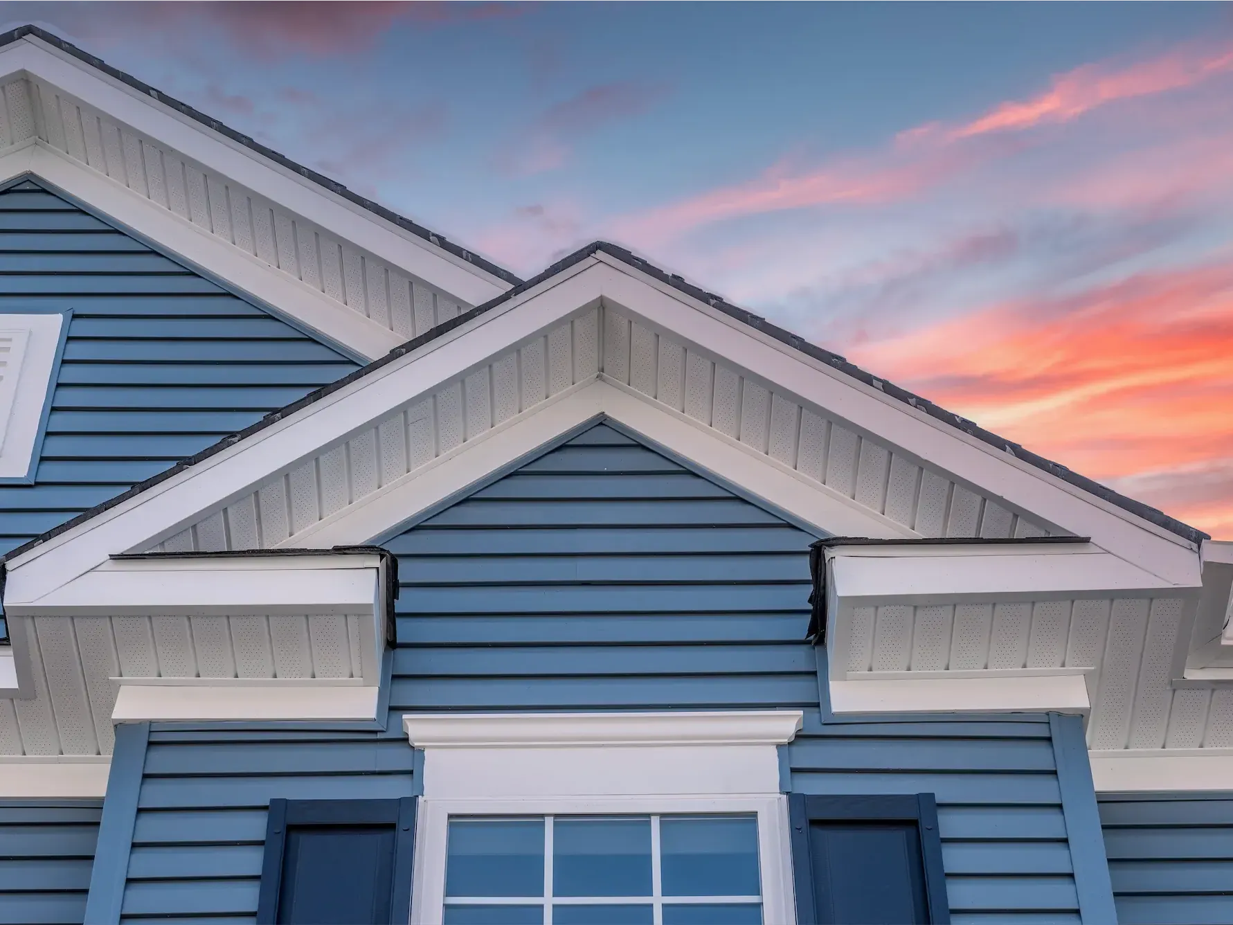 A blue house with a white roof and a sunset in the background