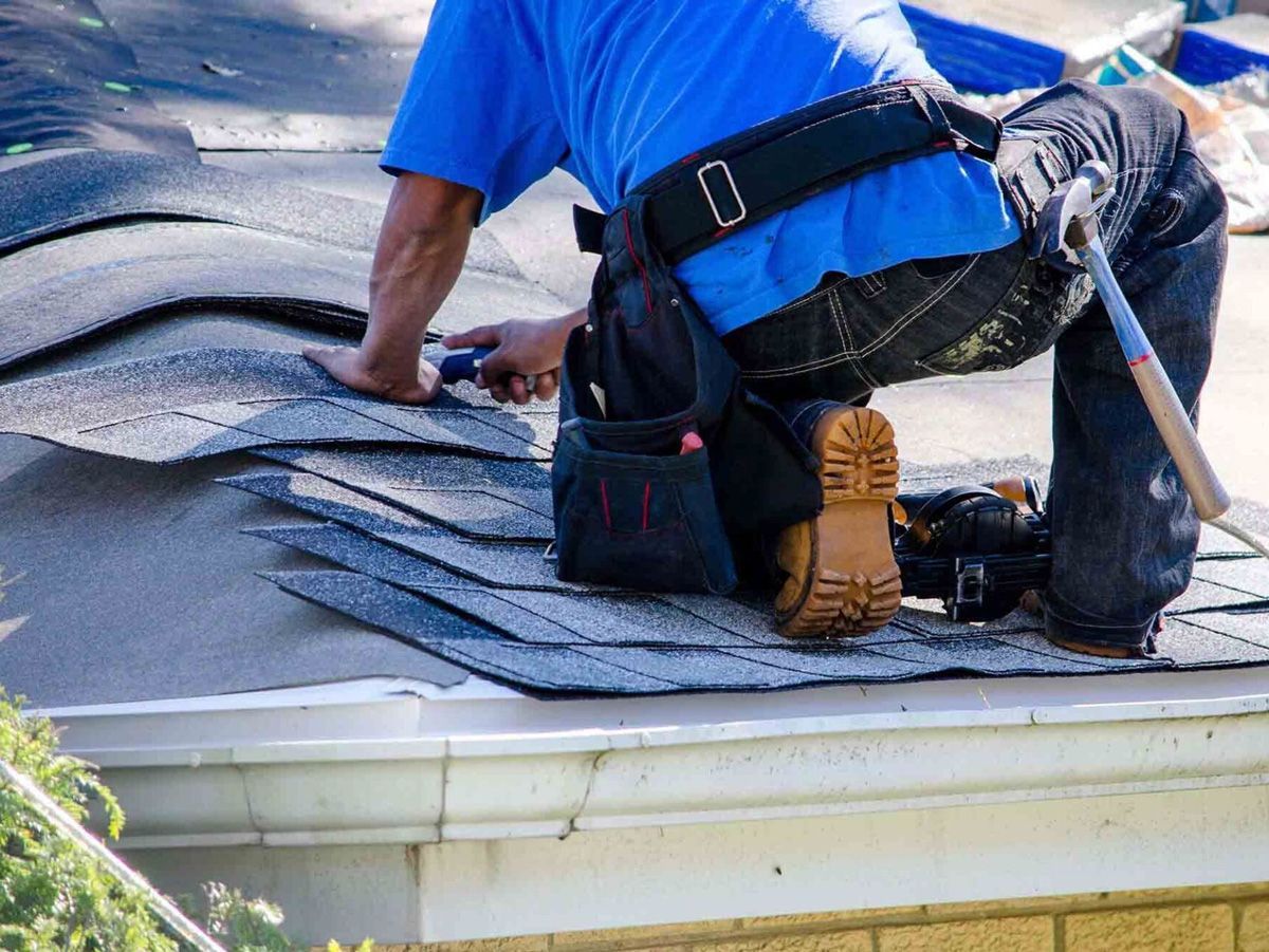 A man is kneeling on the roof of a house.