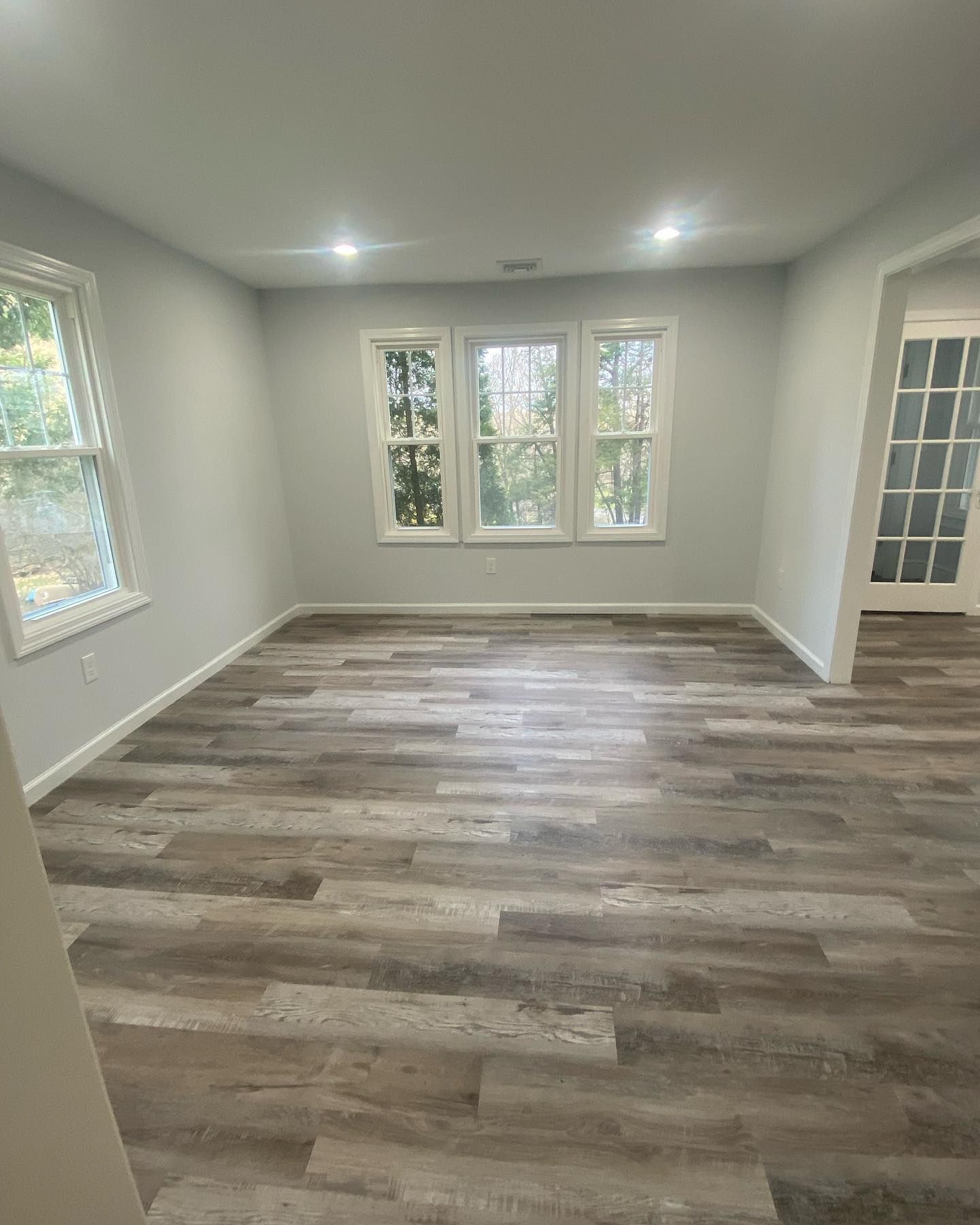 An empty living room with hardwood floors and three windows.