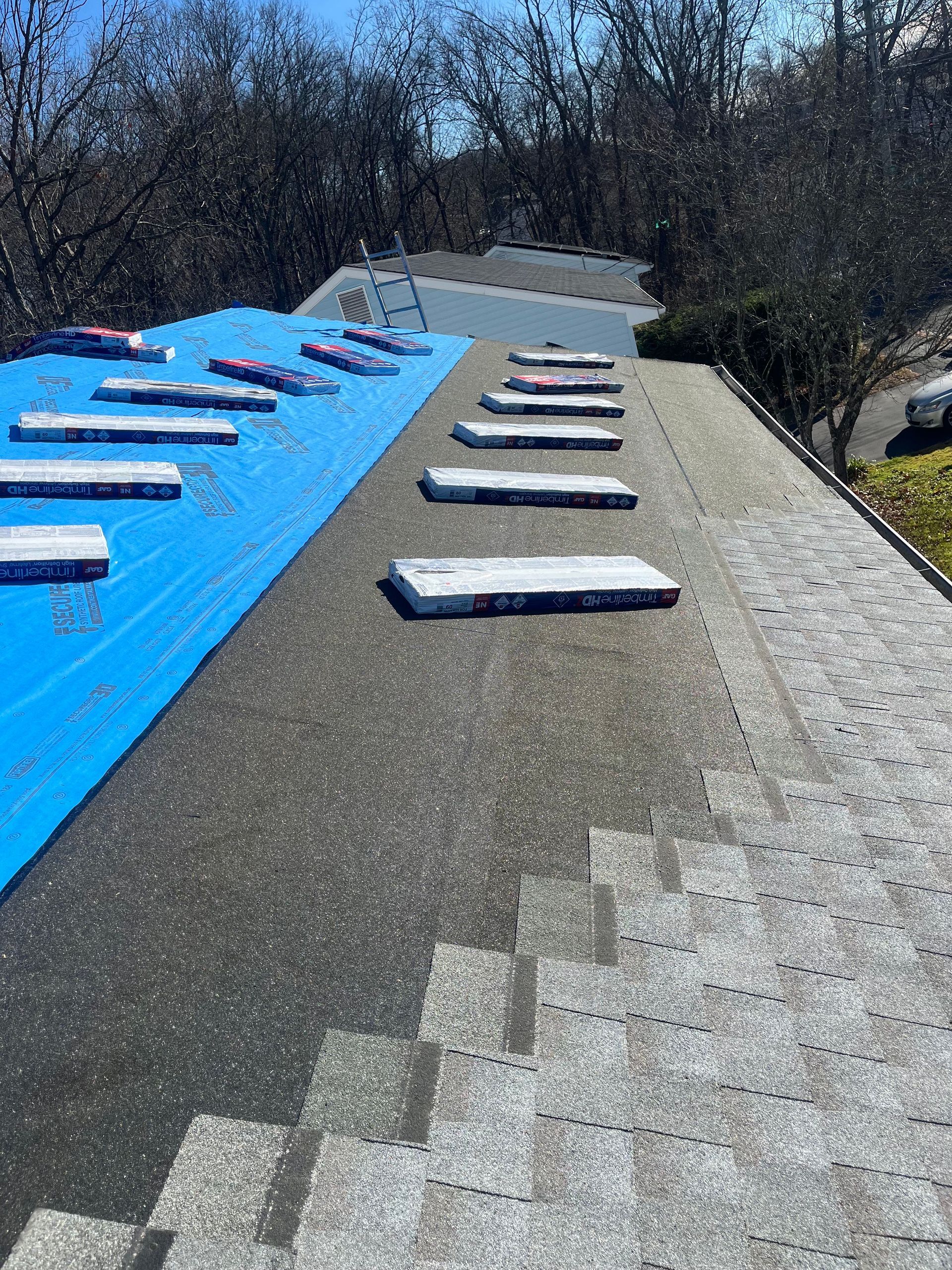 Roof partially covered in blue underlayment and shingles, with unopened shingle bundles.