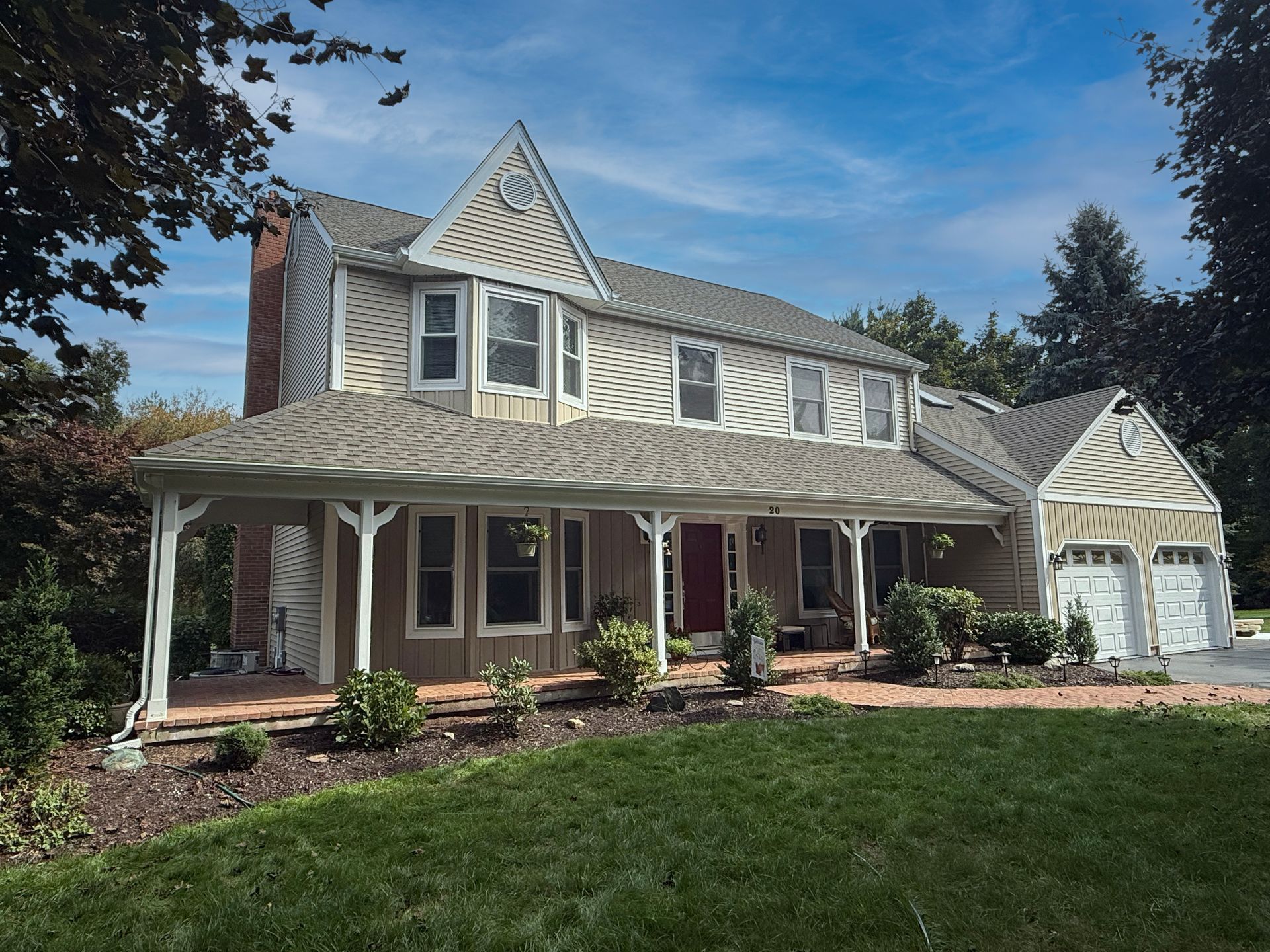 Two-story house with tan siding, a covered porch, and a red front door under a clear blue sky.