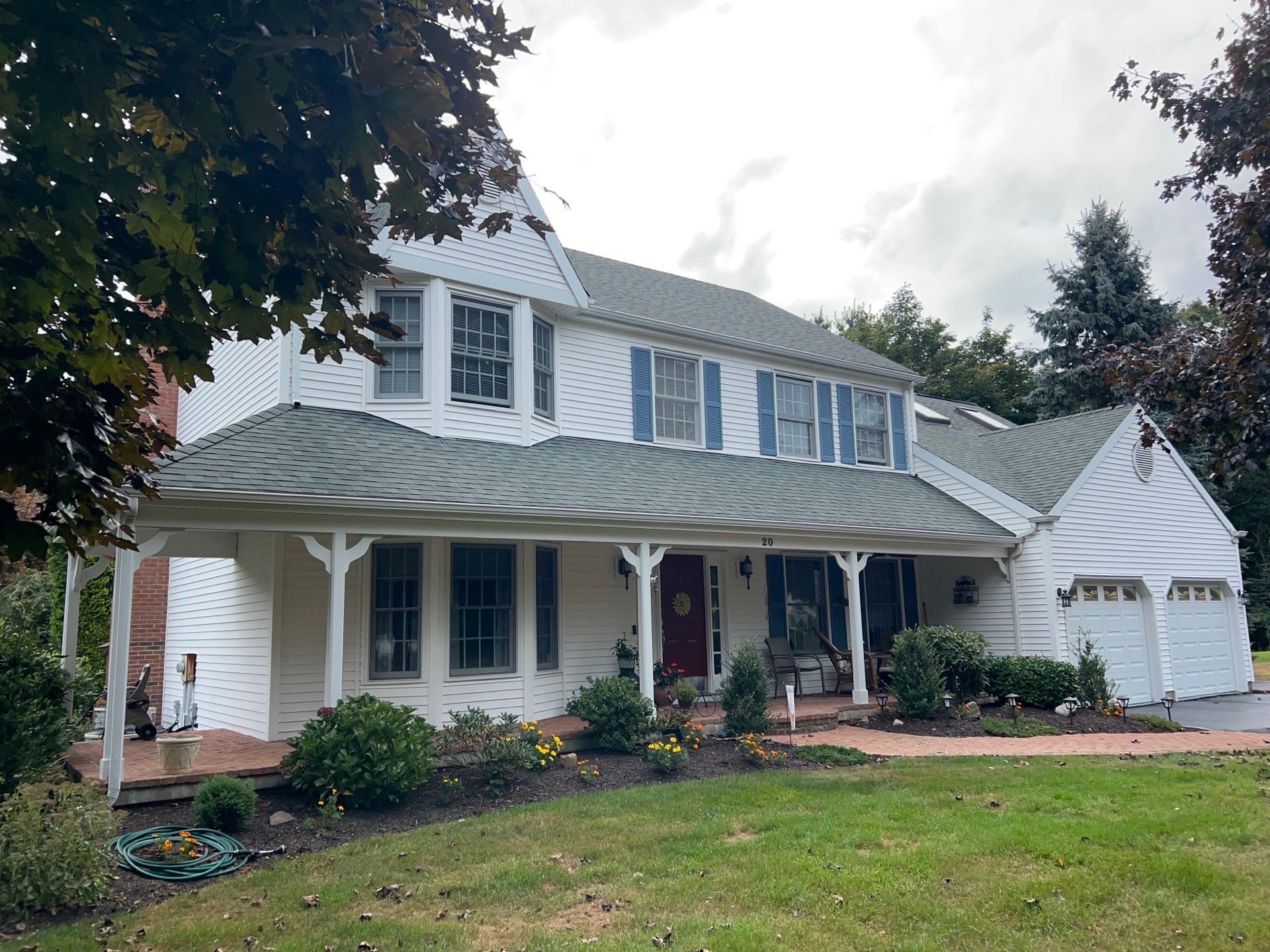 White two-story house with green roof, porch, and attached garage on a grassy lawn under a cloudy sky.