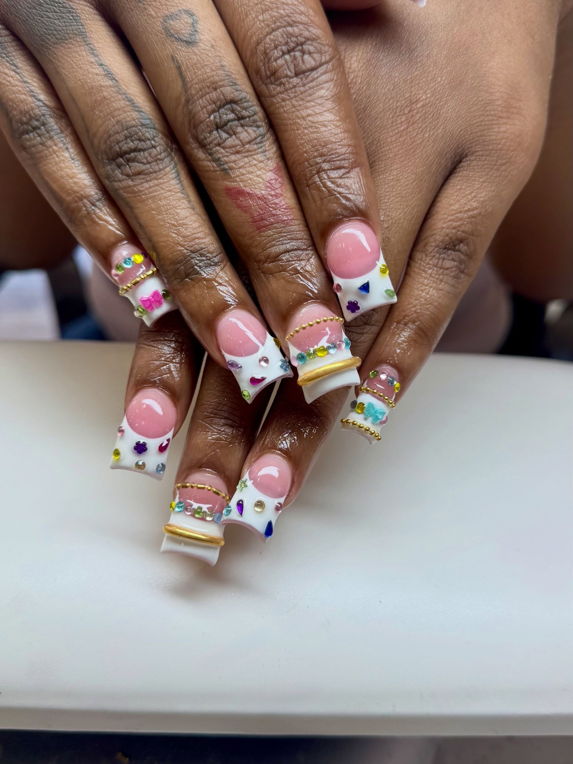 Hands with colorful long nail art resting on a white surface