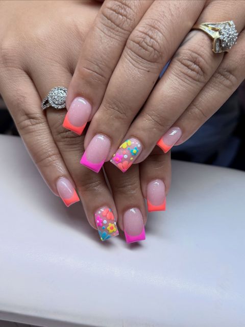 Hands with neon pink ombré nails and colorful floral nail art, wearing rings.