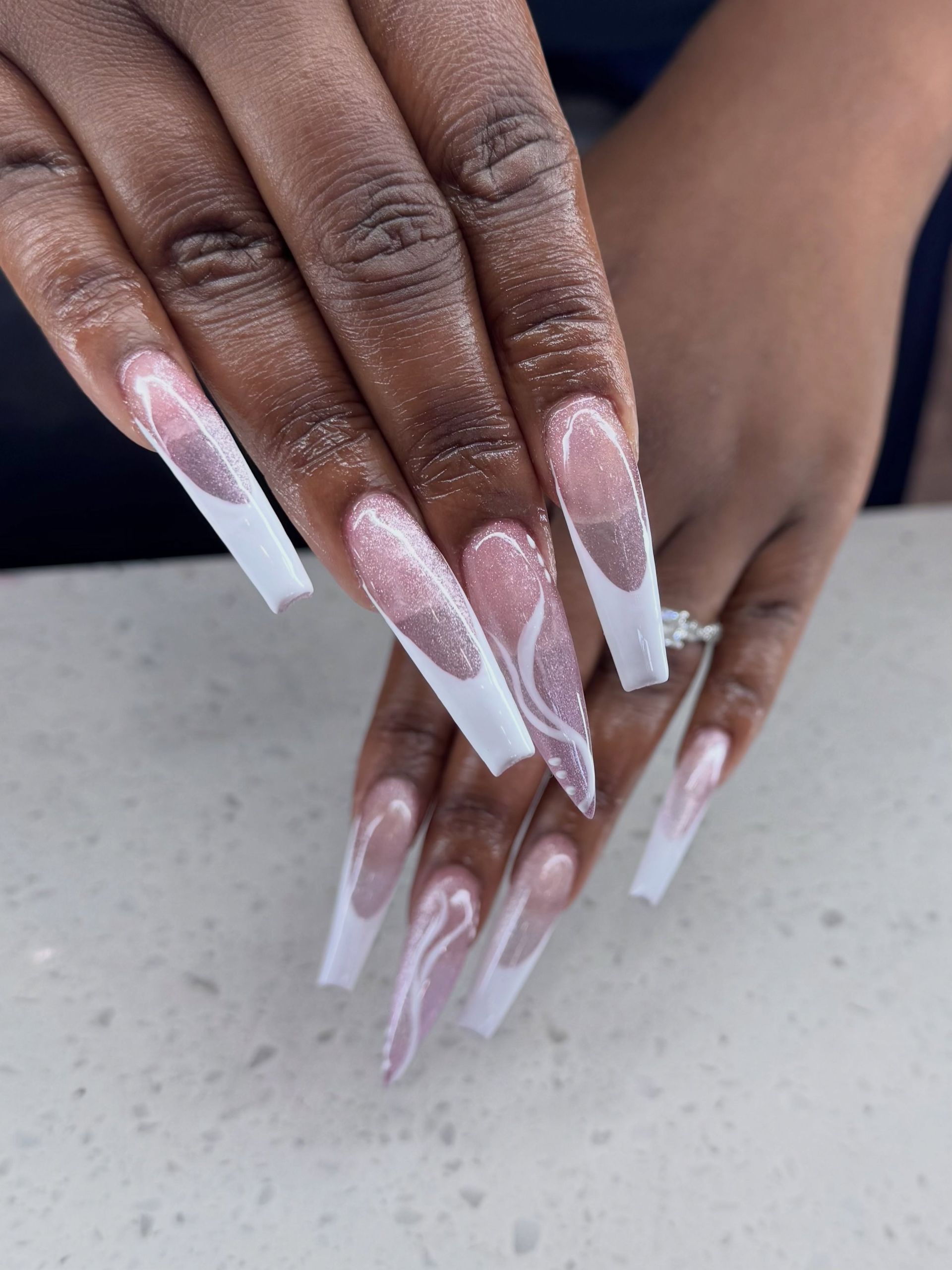 Long white acrylic nails with pink marble design on hands resting together