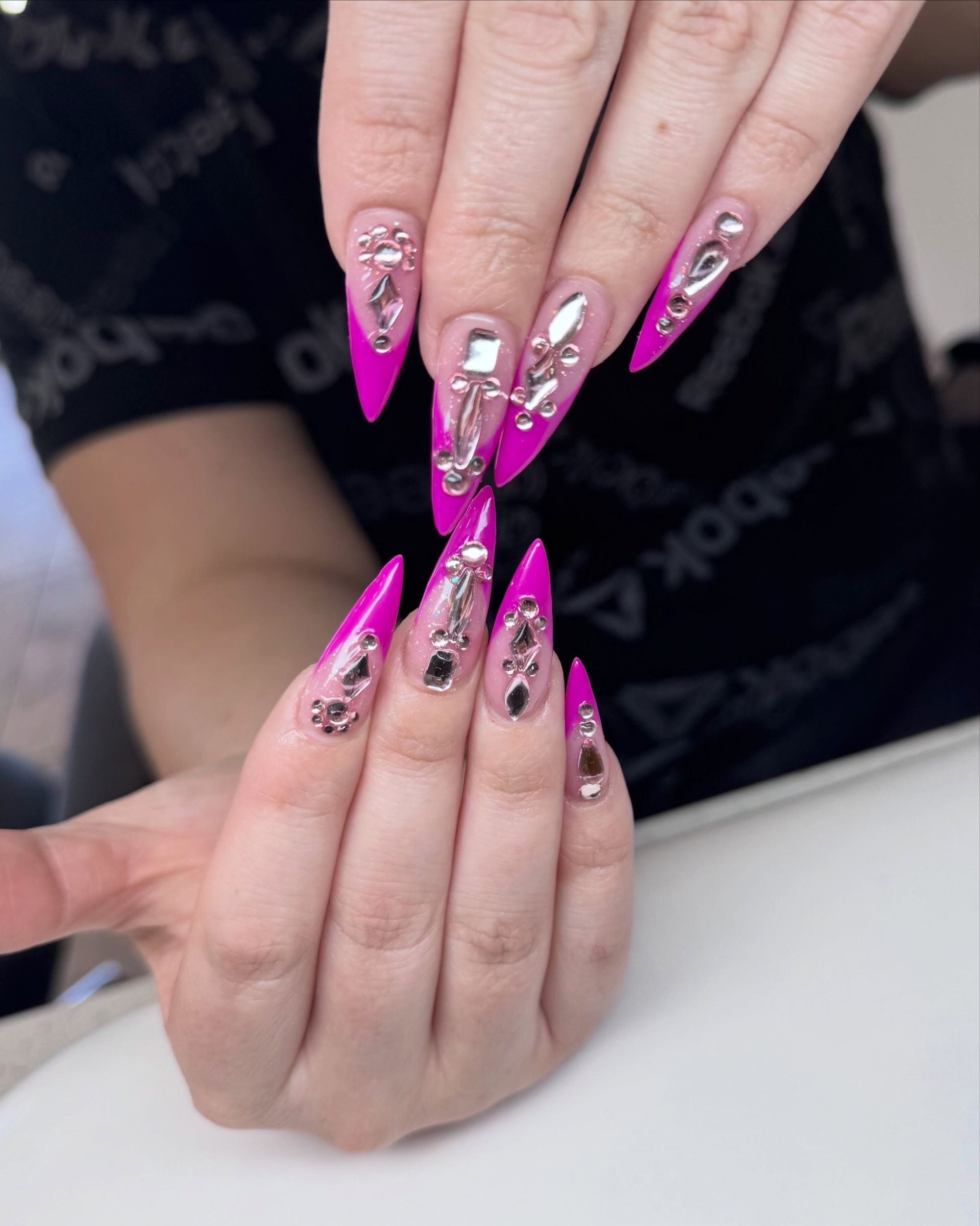 Hands showing long pink and silver rhinestone acrylic nails over a salon table