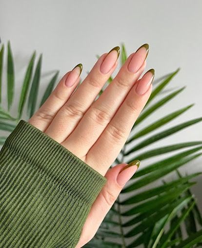 Hand with nude almond nails and green sleeve in front of palm leaves