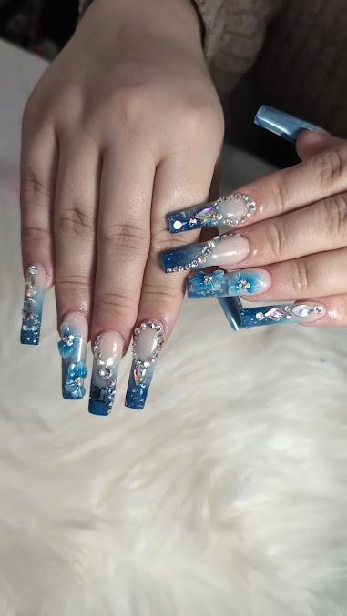 Hands with long blue glitter ombré acrylic nails resting on a white fluffy surface