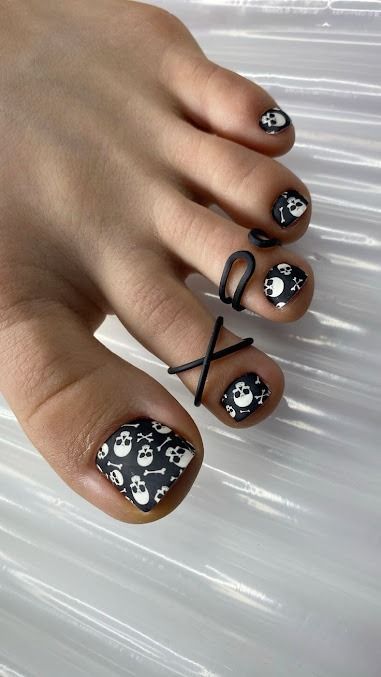 Black floral nail art on toenails, with silver skull accents and black ribbon ties.