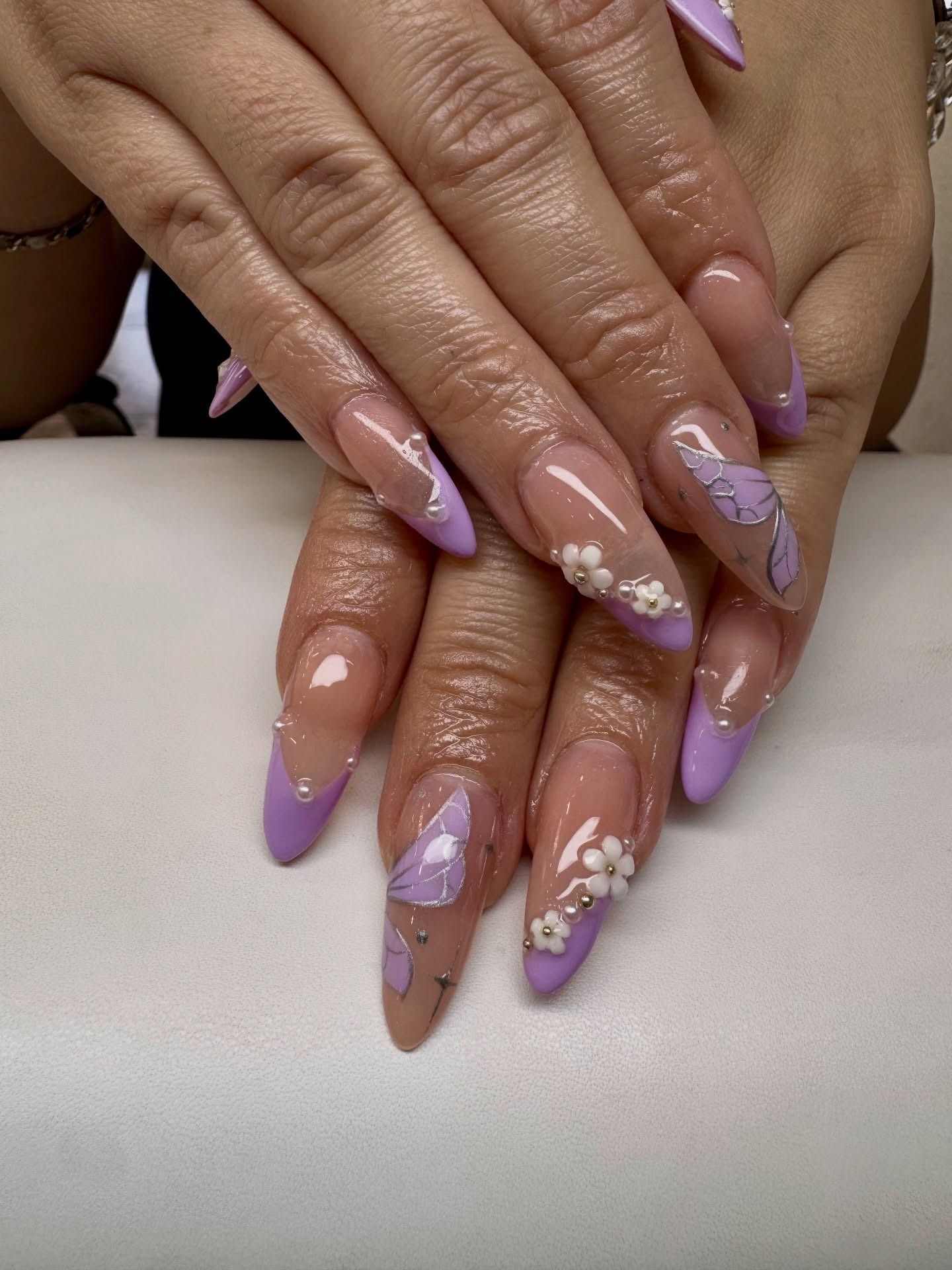 Hands with lavender ombré nails and white floral nail art resting together.