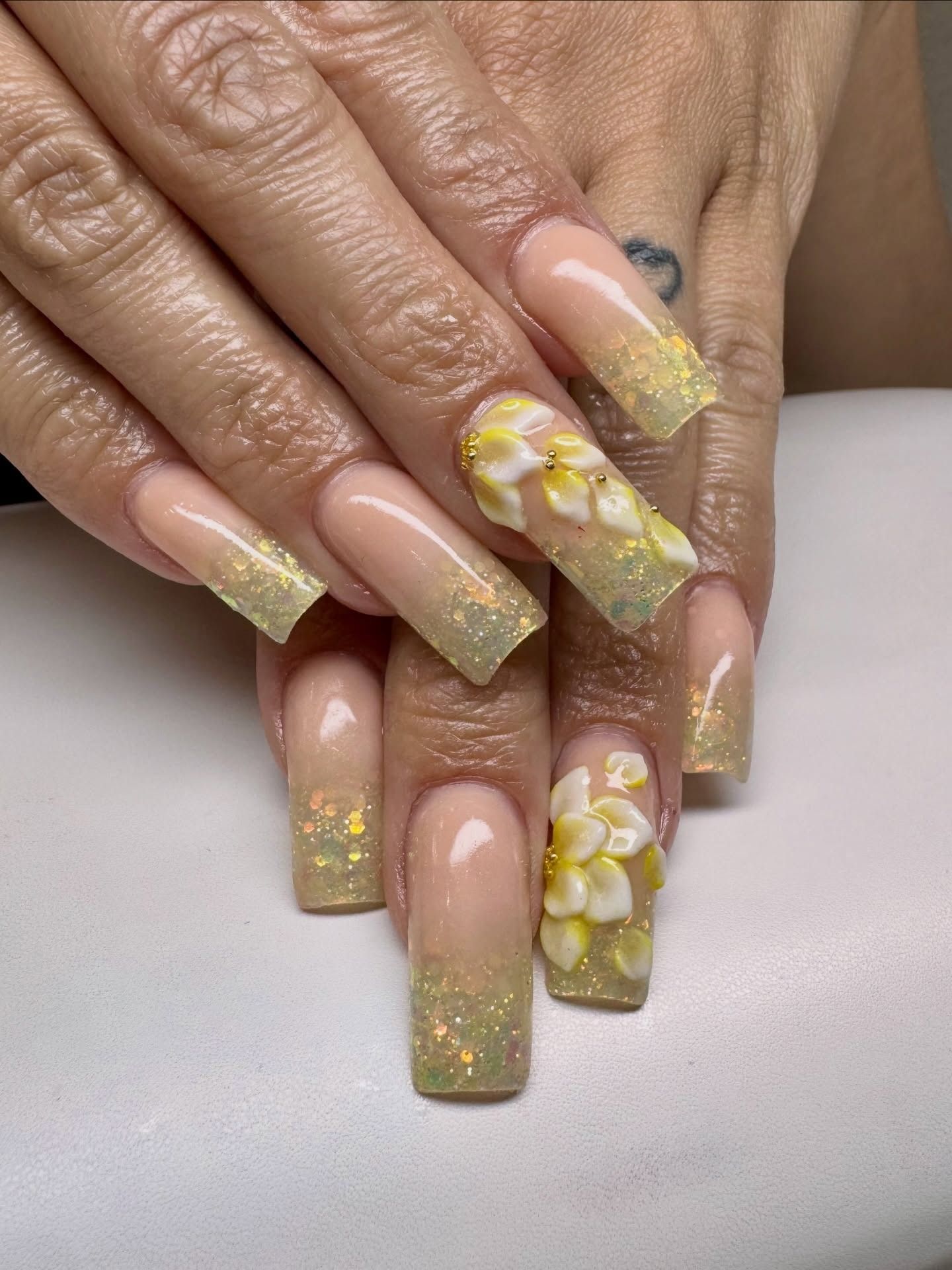 Hands with long yellow glitter and floral acrylic nails resting on a light surface