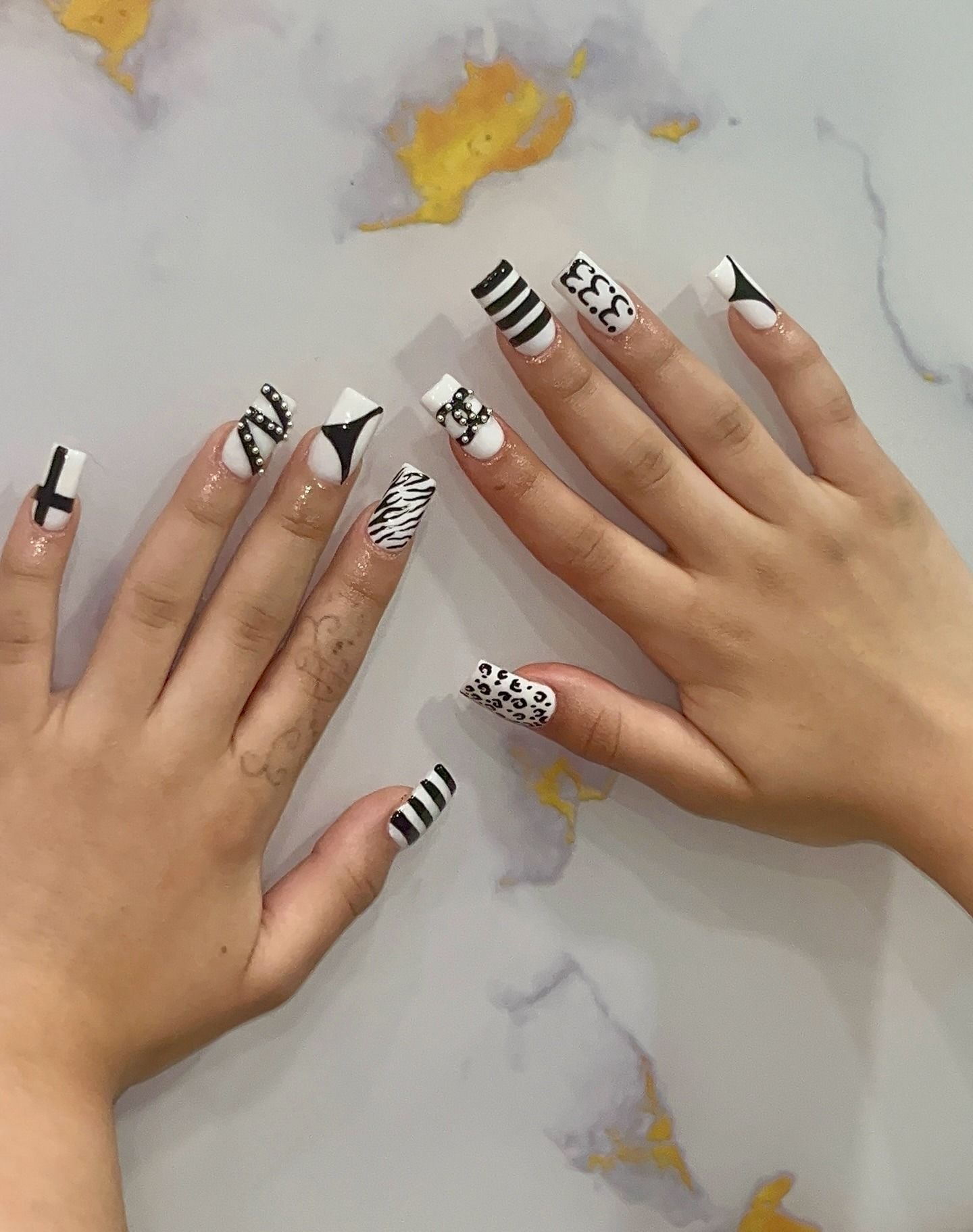 Hands showing black-and-white abstract nail art on a marble surface.