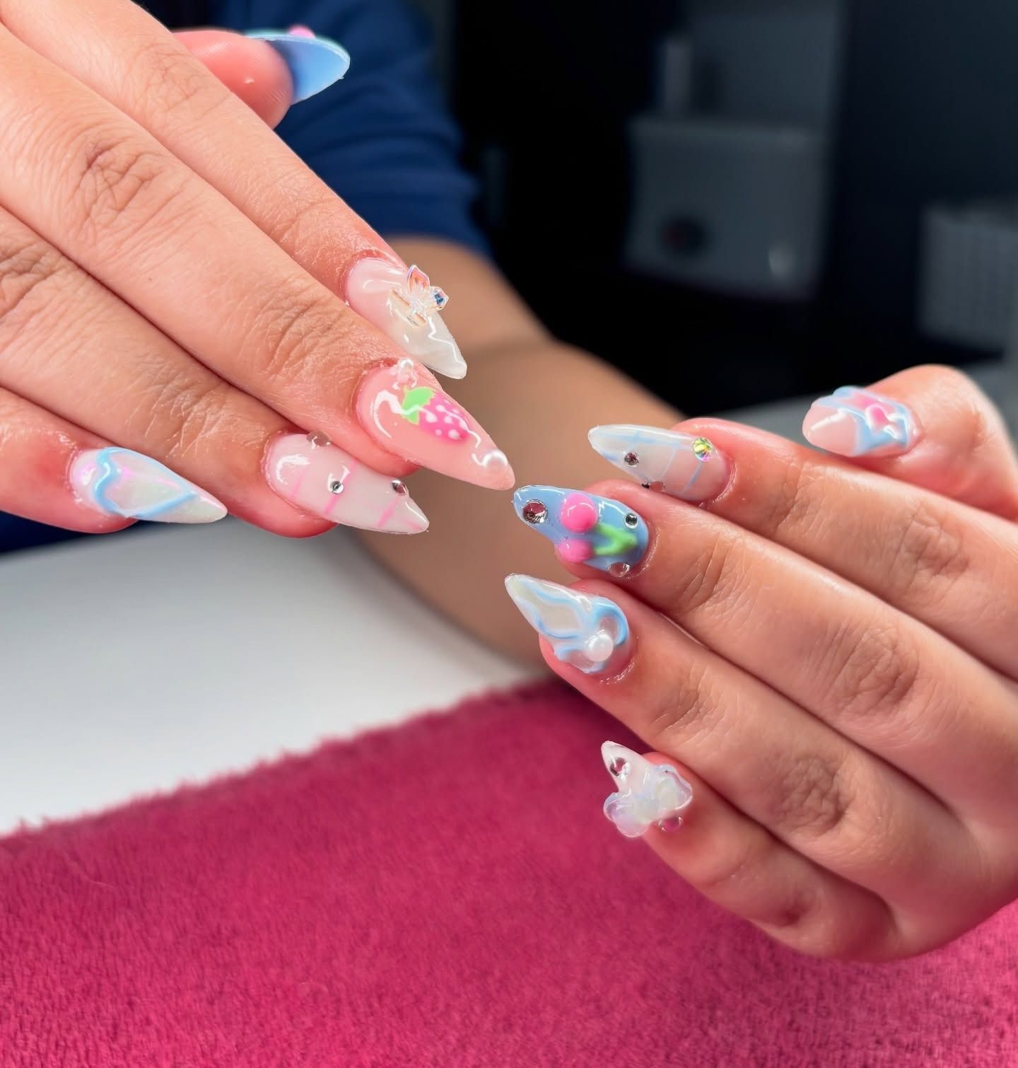 Hands showing long pastel floral acrylic nails over a salon table.