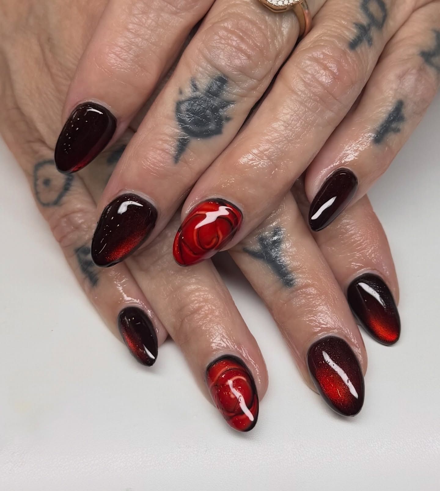Dark burgundy and red coffin nails with glossy swirl nail art on tattooed hands.