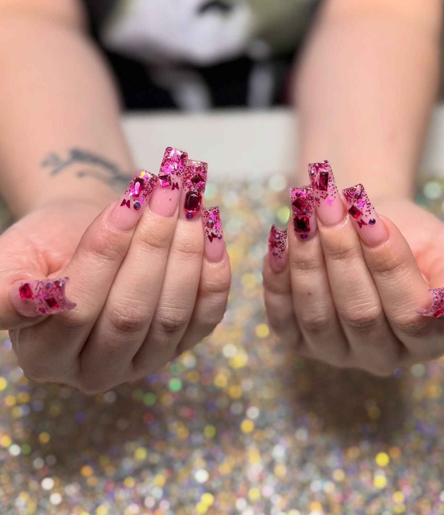 Hands with long pink glitter nails over a sparkly gold surface
