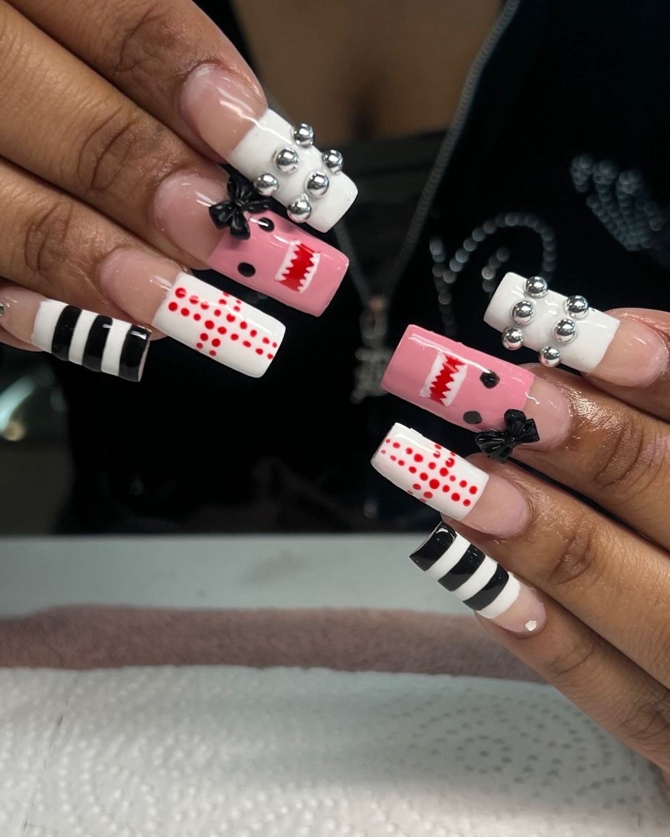 Hands showing long acrylic nails with pink, black, white, and red polka dot nail art.