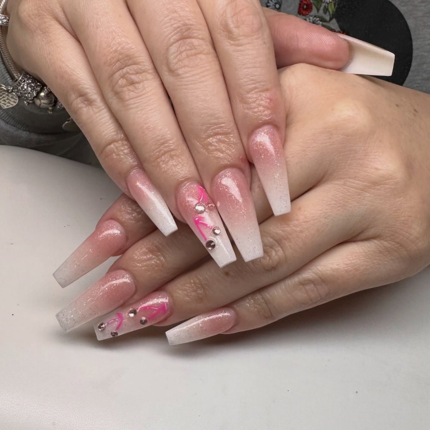 Long ombre pink-and-white acrylic nails with glitter and floral nail art, resting on a hand.