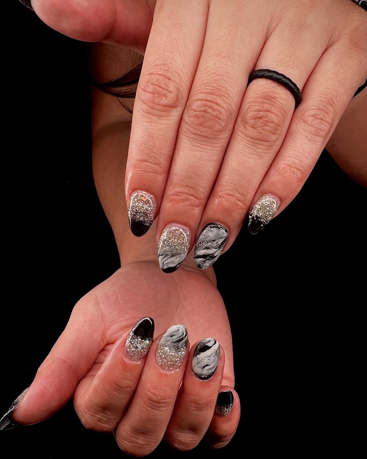 Hands with black and silver glitter nail art, showing manicured nails on a dark background