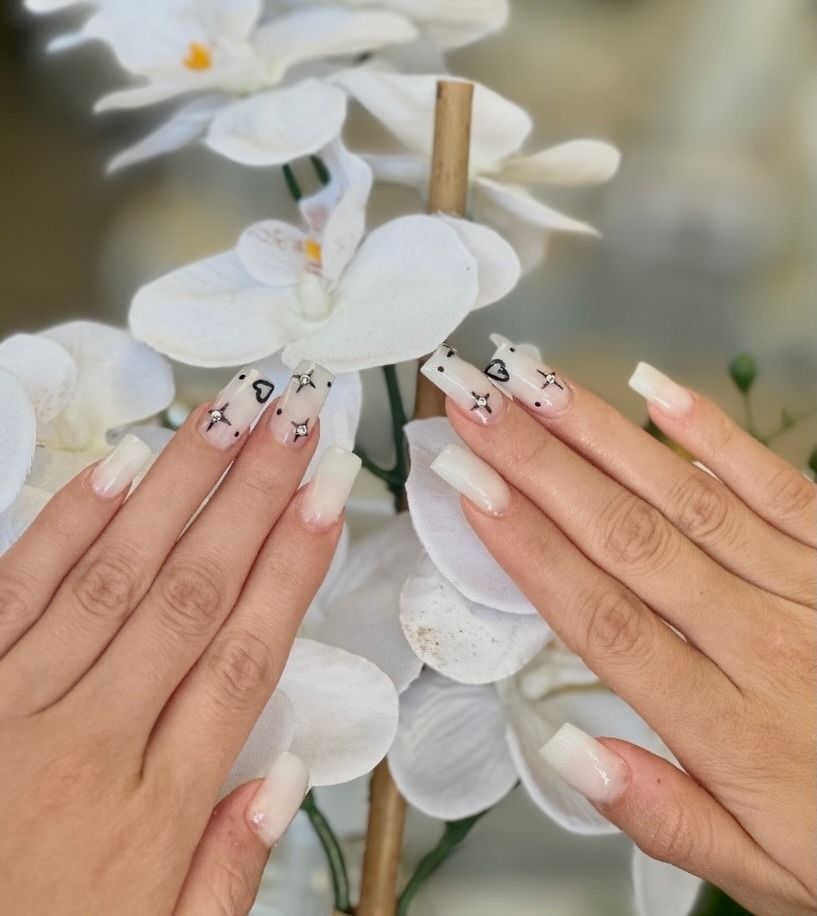 Manicured hands with white floral nail art held before white orchid blossoms.