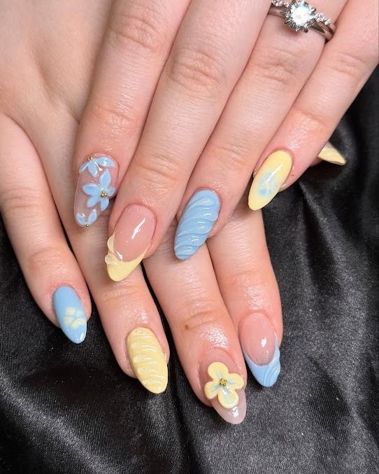Hands with pastel blue, yellow, and pink floral nail art and a silver ring.