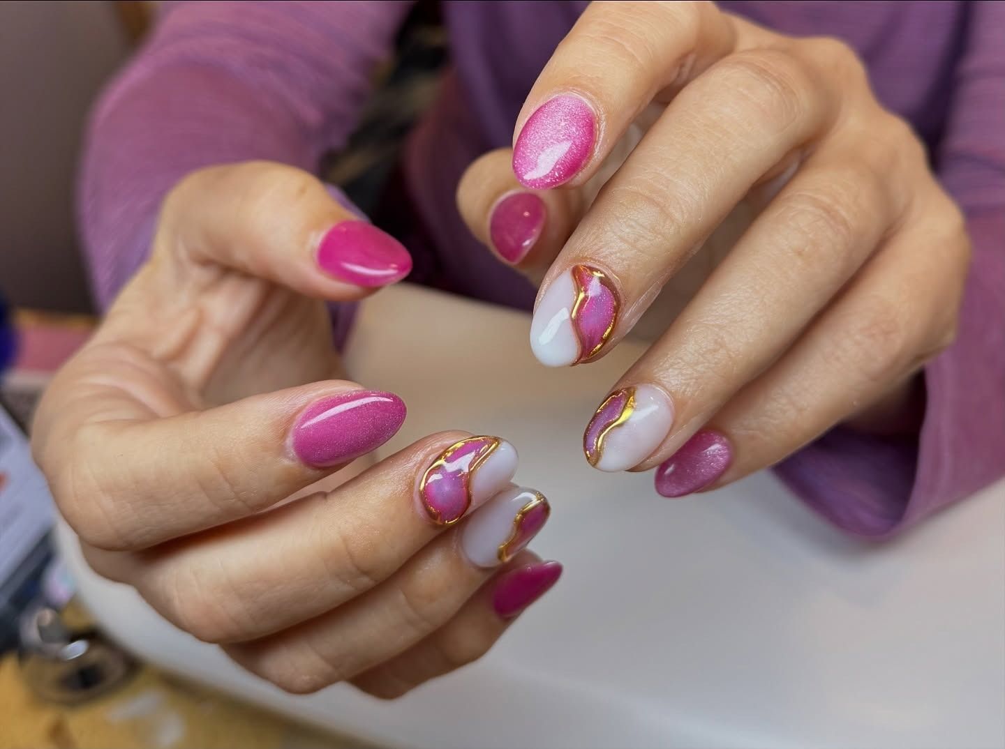 Hands with bright pink and white marbled manicure on a purple background