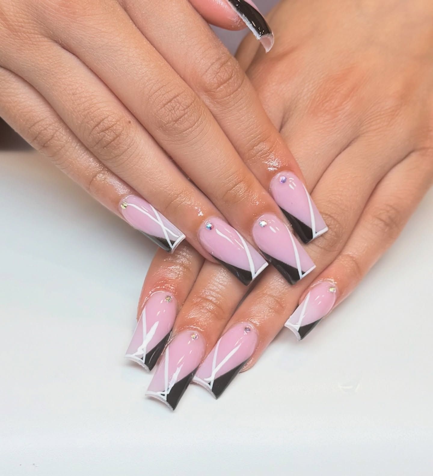 Hands with long pink and black stiletto nails on a white background