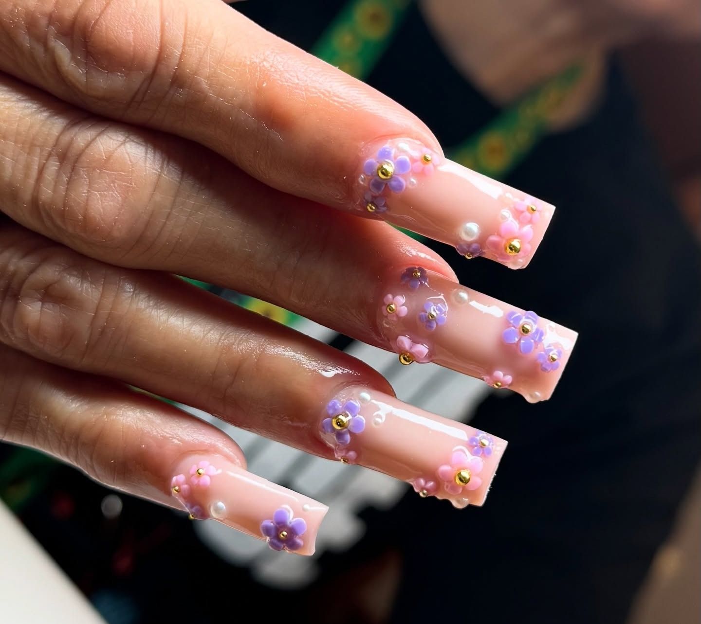 Close-up of hand with long pink acrylic nails decorated with purple and white floral gems